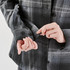 A close-up of a woman's hand adjusting the cuffs of a grey and black plaid shacket featuring buttons.