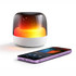 A Dazzle RGB Speaker in white with a glowing gradient light beside a smartphone displaying music controls.