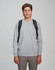 A model wearing a grey long-sleeve shirt and khaki pants, showcasing a black backpack on both shoulders.