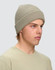A beige cable knit snug beanie displayed on a model, featuring a ribbed design and a logo.