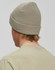 A roll-up cable knit snug beanie in a soft green colour, viewed from the back, featuring a simple logo.