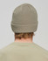A roll-up cable knit snug beanie in a light khaki colour, viewed from the back. Features a ribbed band and a logo.