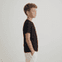 A child stands in profile wearing a black essential tee and white shorts, with hands in pockets.