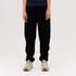 Black track pants with a relaxed fit, paired with beige shoes. The model stands against a plain background.