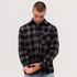 A man wearing a black and grey checkered flannel long sleeve shirt with a pocket, adjusting his cuff.