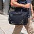 A navy cooler bag with a sturdy strap is being carried by a person walking on a city sidewalk. It has a logo.