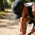 A black sports cap with mesh sides, featuring a logo, worn by a person kneeling on a trail.