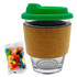 A glass coffee cup with a green lid and cork band, accompanied by a pack of colourful jelly beans.