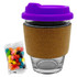A glass coffee cup with a cork band and purple lid, accompanied by a packet of colourful jelly beans.