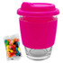 A pink silicone-covered glass coffee cup with a lid, accompanied by a bag of colourful jelly beans.