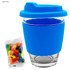A glass coffee cup with a light blue silicone lid and sleeve, accompanied by a pack of colourful jelly beans.