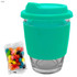 A teal glass coffee cup with a matching silicone lid and sleeve, alongside a bag of colourful jelly beans.