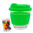 A reusable coffee cup with a clear glass body and a bright green silicone lid and sleeve, alongside a packet of colourful jelly beans.