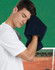 A man in a white shirt wipes his forehead with a dark navy hand towel, set against a green background.