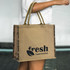 A jute tote bag in natural brown with dark patterned sides and a logo on one side.