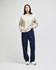 A model wears a beige Champion Reverse Weave® adult crew sweatshirt paired with navy trousers. The sweatshirt has a small logo.