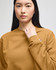 A mustard-coloured crewneck sweatshirt with a logo, worn by a model with long black hair.