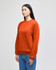 An orange adult crewneck sweatshirt displayed on a model, featuring a logo on the sleeve.