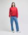 A red crewneck sweatshirt worn by a model with straight black hair, paired with blue jeans and white shoes.