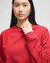 A red crewneck sweatshirt featuring long sleeves and a logo on one sleeve.