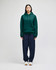 A green hooded sweatshirt with a front pocket, paired with navy trousers, displayed on a model.