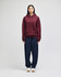 A maroon pullover hooded sweatshirt displayed on a model, paired with navy blue pants. The sweatshirt has a logo.