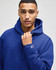 A blue hooded sweatshirt featuring a logo on the sleeve, worn by a model with a neutral expression.