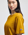 A mustard-coloured Champion adult short-sleeve t-shirt displayed on a model, featuring a small logo on the sleeve.