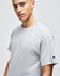 A grey short-sleeve t-shirt featuring a branded logo on the sleeve, displayed by a model.
