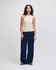 A fitted tank in beige worn with wide-leg denim jeans, featuring a model against a plain background.