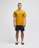 A mustard yellow short sleeve t-shirt displayed on a model, paired with navy shorts. The shirt features a logo.