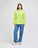 A bright lime green packable anorak jacket with a hood, worn with blue jeans. The model also wears white shoes.