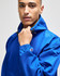 A blue packable anorak jacket worn by a model, featuring a hood and adjustable elements, with a logo on the sleeve.