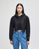 A black cropped hoodie with a hood and long sleeves, worn with blue jeans. It features a logo on one sleeve.