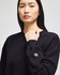 A black women's crewneck sweatshirt with a logo on the sleeve. The model is posing with a serious expression.