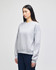 A grey women's crewneck sweatshirt with long sleeves and a logo on the sleeve, displayed on a model.