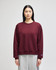 A maroon women's crewneck sweatshirt with a relaxed fit and a logo on the sleeve, paired with grey sweatpants.