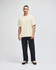 A beige Champion Adult Heritage Jersey T-Shirt worn by a model, paired with black trousers and casual shoes.