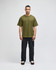 A green Champion Adult Heritage Jersey T-Shirt worn by a model, paired with black pants. The shirt features a logo.