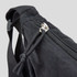 A black bag featuring a zip closure and adjustable strap, with a woven texture. It includes a logo on the side.