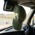 A green vintage washed cap hanging from the mirror inside a vehicle, with a logo on the front.