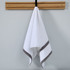 A white hand towel with grey stripes, hanging from a wooden rack against a light wall. Features a logo.