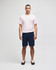 A man stands wearing a pink t-shirt and navy cotton gym shorts, featuring a logo on the shorts.