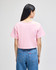 A pink cropped short sleeve t-shirt with a simple design, featuring a branding logo on the back.