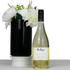 A bottle of white Sauvignon Blanc wine beside a black vase with white flowers. The bottle has a label and branding.