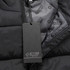 A black unisex puffer vest with a zip and an inner lining featuring a branding logo. A tag is attached.