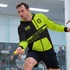 A man wearing a black and bright green zipped hoodie is playing squash. The hoodie features a logo and sporty design.