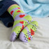 A pair of green and lilac socks with heart patterns and grip dots on the soles, resting on a bed.