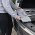 A person placing a grey and black premium foldable cooler into a car boot, showcasing its compact design.