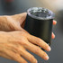 A drink bottle in matte black with a clear lid, held in a person's hand, featuring a logo.